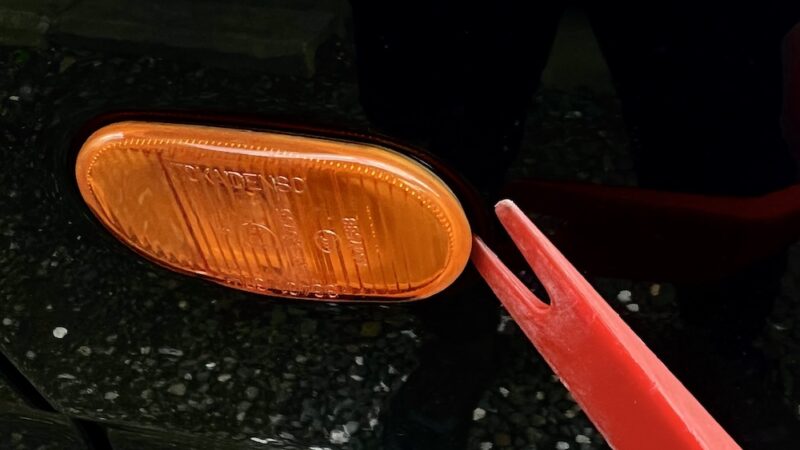 サイドマーカーランプの隙間に内張り剥がしを差し込み取り外す様子