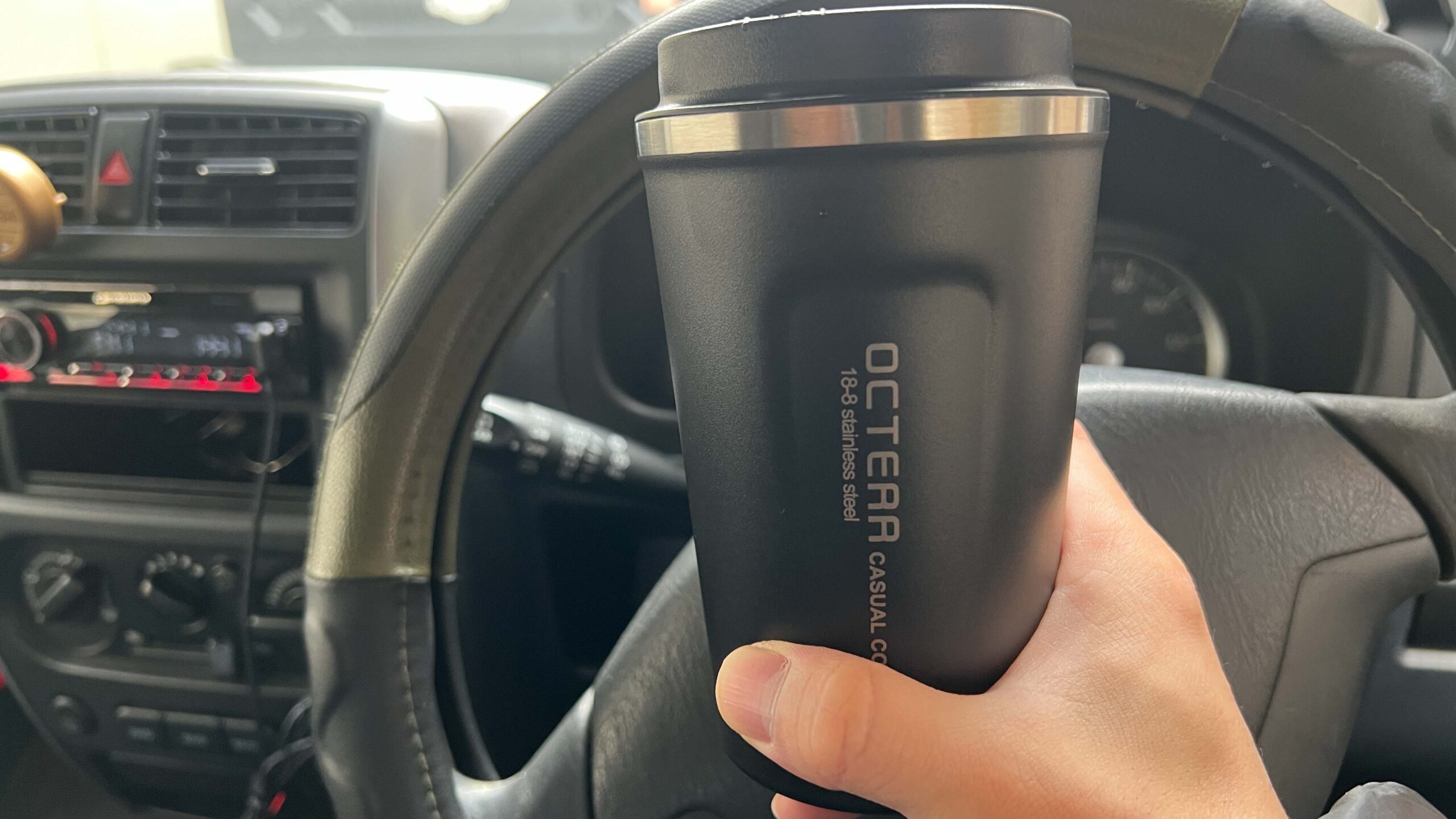 運転席でタンブラーを手に取る様子。車内でも使いやすいサイズ感